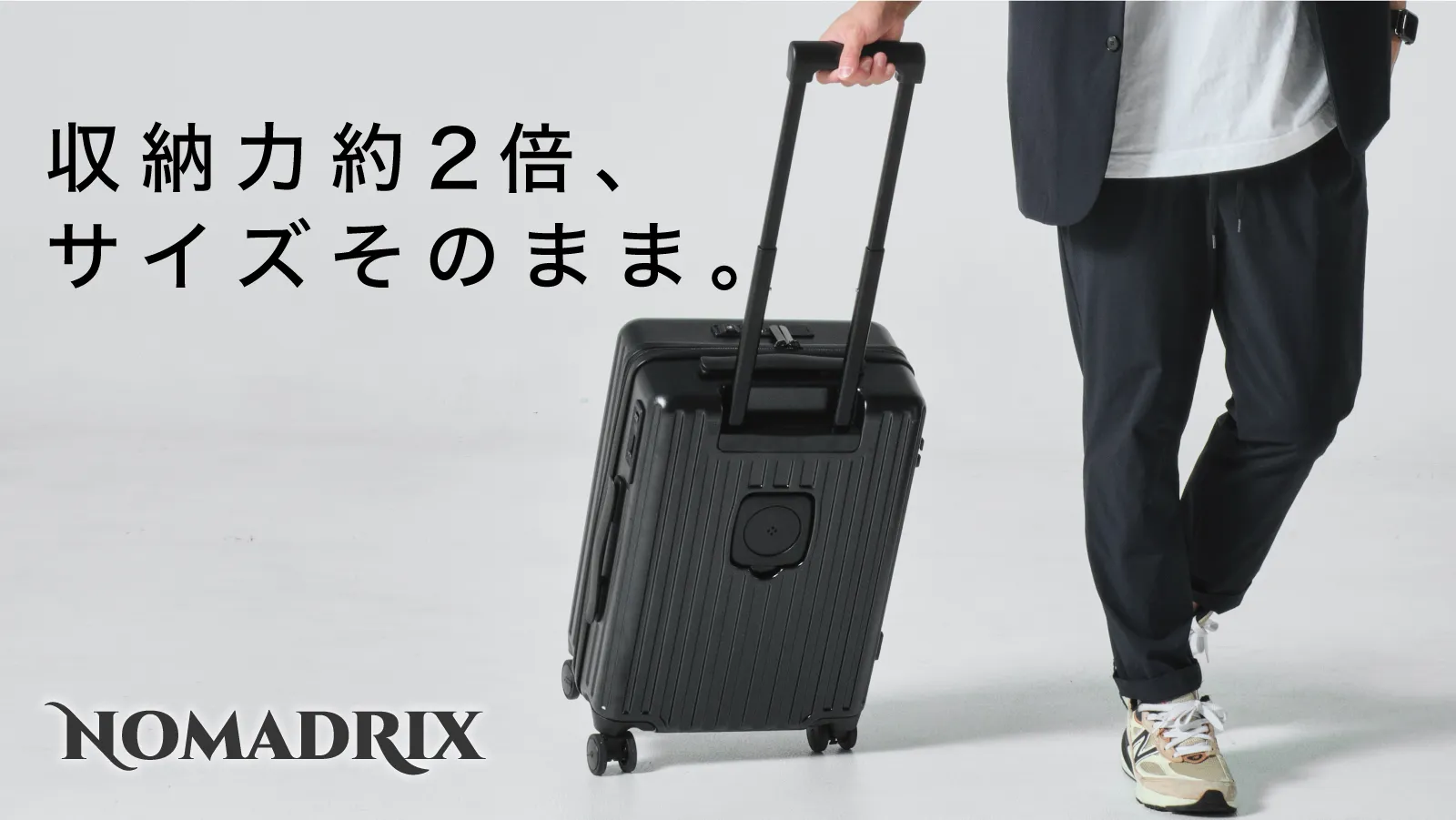 NOMADRIXのスーツケース広告。「収納力約２倍、サイズそのまま。」と記載され、黒いキャリーケースを引く男性が写っている。